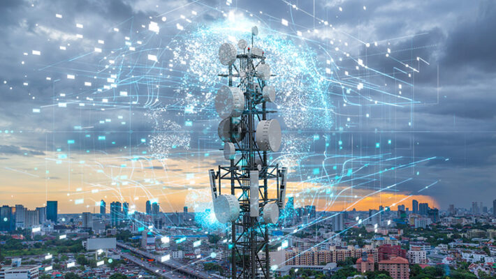 Telecommunications tower with numerous antennas set against a city skyline at dusk.