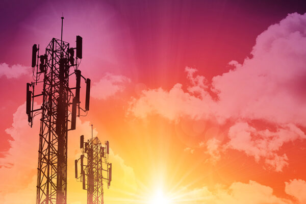 Two telecommunications towers against a vibrant orange and pink sunset with scattered clouds.