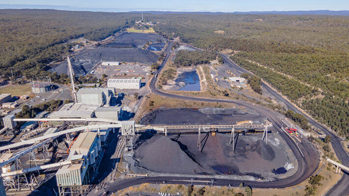 Aerial view of an industrial mining site, featuring conveyor belts, large buildings and surrounding forested areas.