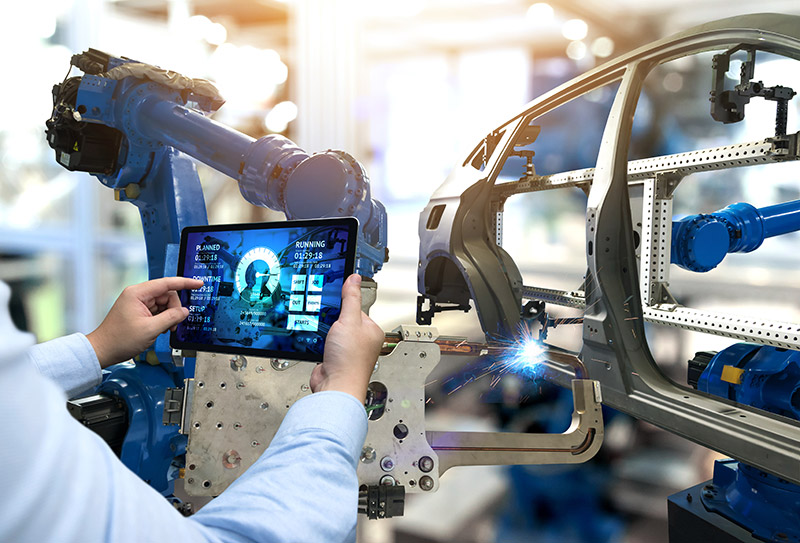 In an industrial setting, a person uses a tablet connected via private 5G to analyze robotic arms welding a car frame seamlessly.