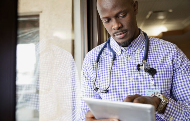 A doctor wearing a stethoscope around their neck using a tablet.