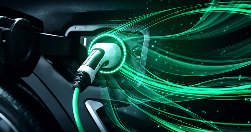 Close-up of an electric vehicle charging with a glowing green plug connected to the port and emitting striking light trails.
