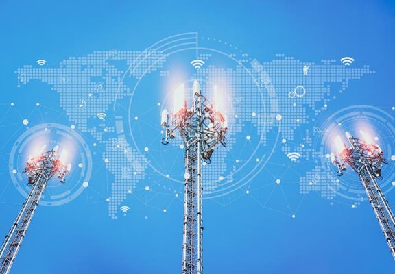 Three telecommunications towers with signal lights are set against a backdrop of a world map and connectivity icons.