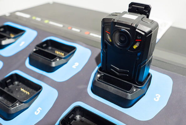 The body-worn camera rests in charging dock three, amid empty blue charging slots marked by numbers.